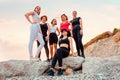 Bottom view of group of Caucasian beautiful women wearing sportswear posing at rocks. Sea and sunset in background
