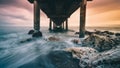 Bottom view of a rocky coast boarding an old wooden pier during a dramatic sunset Royalty Free Stock Photo