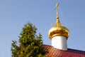 Bottom view of shiny christian church dome with cross on top on red roof against tree and sky Royalty Free Stock Photo