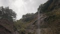 Bottom view of a small waterfall and a steep cliff on cloudy sky background. Action. Beautiful green mountain slope and Royalty Free Stock Photo