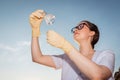 Bottom view of woman ecologist wearing rubber gloves and eyeglasses examines test flask of water. Concept of ecology and