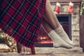 Bottom view of woman legs in knitted winter socks sitting on armchair covered plaid near christmas tree and fireplace. Bottom view