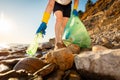 Bottom view of woman volunteer& x27;s hand in rubber gloves takes plastic bottle from pebble wild coast. Concept of ocean