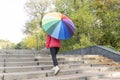 Bottom view of young female with big multicolored umbrella coming outdoor upstairs