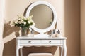 Boudoir women\'s white table for makeup with a bouquet of flowers and a mirror on the background of a beige wall.