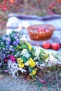 Bouguet of flowers lying on grass, basket with fruits on blanket in background.