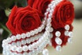 Bouguet of red roses with green leaves, with a necklace of white pearls and scattered beads reflected in the mirror closeup.