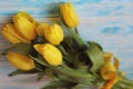 Bouguet of yellow tulips tied with yellow satin ribbon on blue wooden background close-up.