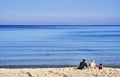 Boujaafar beach in winter with blue skies and sunshine with a young family of a mother, father and child sitting on the sand