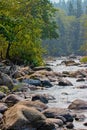 Boulders and large rocks rise out of wide flat river in summer