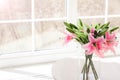 Bouquet of artificial flowers in a glass vase on a white table in front of a large window Royalty Free Stock Photo