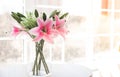 Bouquet of artificial flowers in a glass vase on a white table in front of a large window Royalty Free Stock Photo