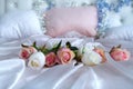 A bouquet of artificial flowers lies on a white silk blanket on a large bed.