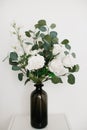 Bouquet of artificial plants and white flowers in vase, stands on light background. Royalty Free Stock Photo