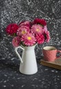 Bouquet of autumn flowers asters in a white jug, book and a mug of tea on a dark background.