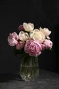 Bouquet of beautiful peonies in glass vase on dark table against black background Royalty Free Stock Photo