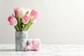 Bouquet of beautiful spring tulips in vase and gift box on marble table against light background.