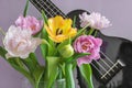 A bouquet of beautiful tulips on a lilac background and a fragment of a musical instrument ukulele.