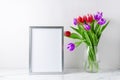 Bouquet blooming red purple white tulip flowers in glass vase and empty poster or photo frame mockup on white marble table in Royalty Free Stock Photo