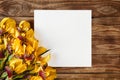 A bouquet of blooming yellow irises and white sheet of paper on a wooden background. Flat layout with space for text Royalty Free Stock Photo