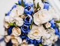 A bouquet of the bride from white and blue roses and wedding rings from gold Royalty Free Stock Photo