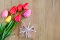 A bouquet of bright colorful tulips and a gift box on a wooden background. Copy space Royalty Free Stock Photo