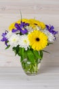 A bouquet of bright flowers in a glass jug on a light wooden background. Still life in a rustic style. Yellow gerbera, blue iris Royalty Free Stock Photo