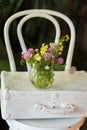 Bouquet of bright wild flowers in a glass vase on a suitcase lying on a wooden white chair Royalty Free Stock Photo