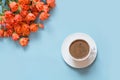 Bouquet of bush orange roses and cup of black coffee on pastel blue background. Flat lay. Copy space.