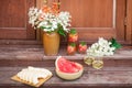 Bouquet in clay vase, watermelon, watermelon lemonade, white wine and melon are on steps of rustic wooden ladder