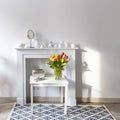 Bouquet of colorful tulips in a glass figured vase on a white fireplace console. A faience figurine of angel as an interior