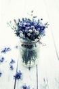 Bouquet of cornflowers in a glass jar on a white wooden table close-up. Wild blue summer flowers in a vase Royalty Free Stock Photo