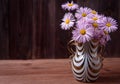 Bouquet of daisies with lilac petals in a glass vase on a wooden table