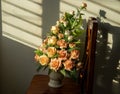 Bouquet of fake artificial roses in a vase set on a wooden chair with louvered sunlight. Royalty Free Stock Photo