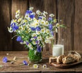 Bouquet of field flowers, glass of milk and soft bread on the wooden table. Royalty Free Stock Photo