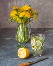 A bouquet of the first primroses in a glass jug and a soft drink with lemon and lemon balm. Blooming dandelions, canola and sprigs Royalty Free Stock Photo