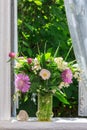 A bouquet of flowers of clover, cornflowers and Jasmine in a glass vase and a heart shaped stone on the windowsill of an open wind Royalty Free Stock Photo