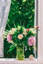 Bouquet of flowers of clover, cornflowers and Jasmine in a glass vase and a heart shaped stone on the windowsill of an open window Royalty Free Stock Photo