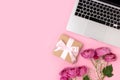 Bouquet of flowers, laptop and gift box with tied bow on a pink background.