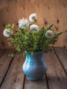 Bouquet of fluffy dandelions and spike wild herbs in a blue vase