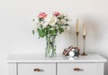 Bouquet of fresh chrysanthemum and carnations, candles in brass candlesticks, photo camera on a white cabinet in the living room