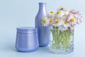 A bouquet of fresh flowers, daisies on green stems are in a glass with clean water and two purple jars with cream cosmetics on a Royalty Free Stock Photo