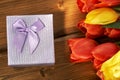 Bouquet of fresh tulips illuminated by sun ray and a gift box lying on the wooden table. Royalty Free Stock Photo