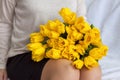 A bouquet of fresh yellow tulips lies on the lap of a young girl. The legs of a girl in knitted knee socks. The concept of spring