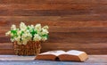 Bouquet of Jasmine flowers in a woven straw basket and an open book on a table on a brown wooden retro background Royalty Free Stock Photo