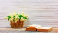 A bouquet of Jasmine flowers in a woven straw basket and an open book on a table on a white wooden retro background Royalty Free Stock Photo