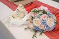 A bouquet of light roses hand flowers beside a teddy bear couple soft toy display displayed on a table with red cloth for weddings