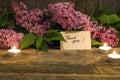 bouquet of lilac, candle and thank you card on old wooden background closeup.