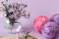 A bouquet of lilac chrysanthemums in a glass vase with skeins of multicolored yarn, close - up-the concept of needlework in autumn
