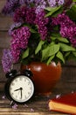 Bouquet of lilac flowers in a ceramic pot with a black alarm clock Royalty Free Stock Photo